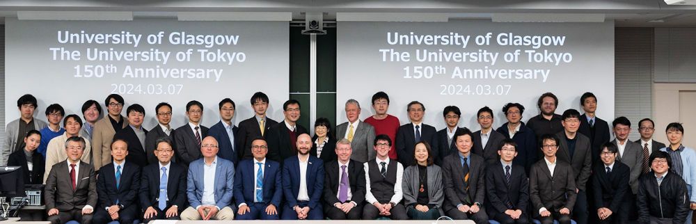 Glasgow and Tokyo delegates in a group photo in front of a sign saying University of Glasgow, University of Tokyo 150th Anniversary 2024.03.07