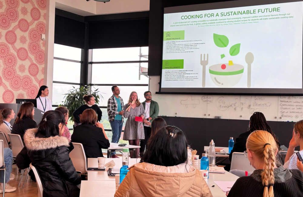 Five students presenting in front of a classroom of students with a presentation slide about cooking for a sustainable future