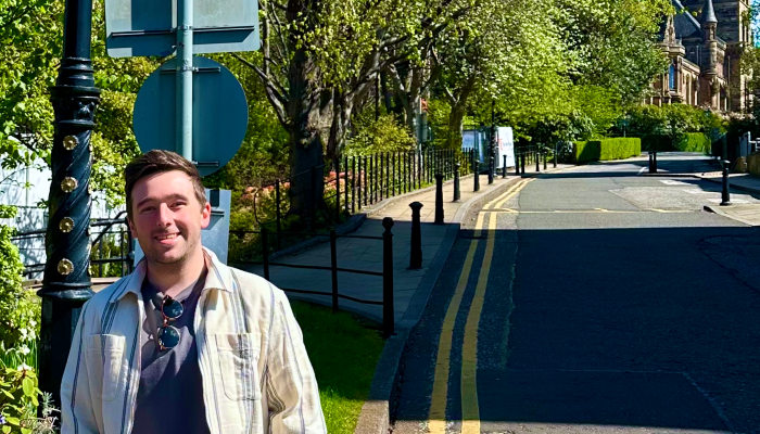 Dr Liam Rooney stood on the pavement, with the Sir Gilbert Scott Building in the background