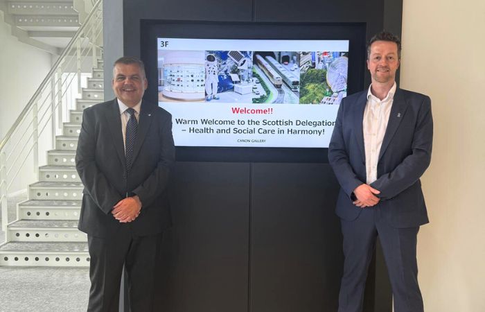 Two men posing in front of a TV screen