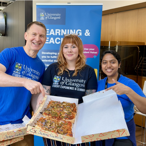 Three staff members smile holding pizzas for the event