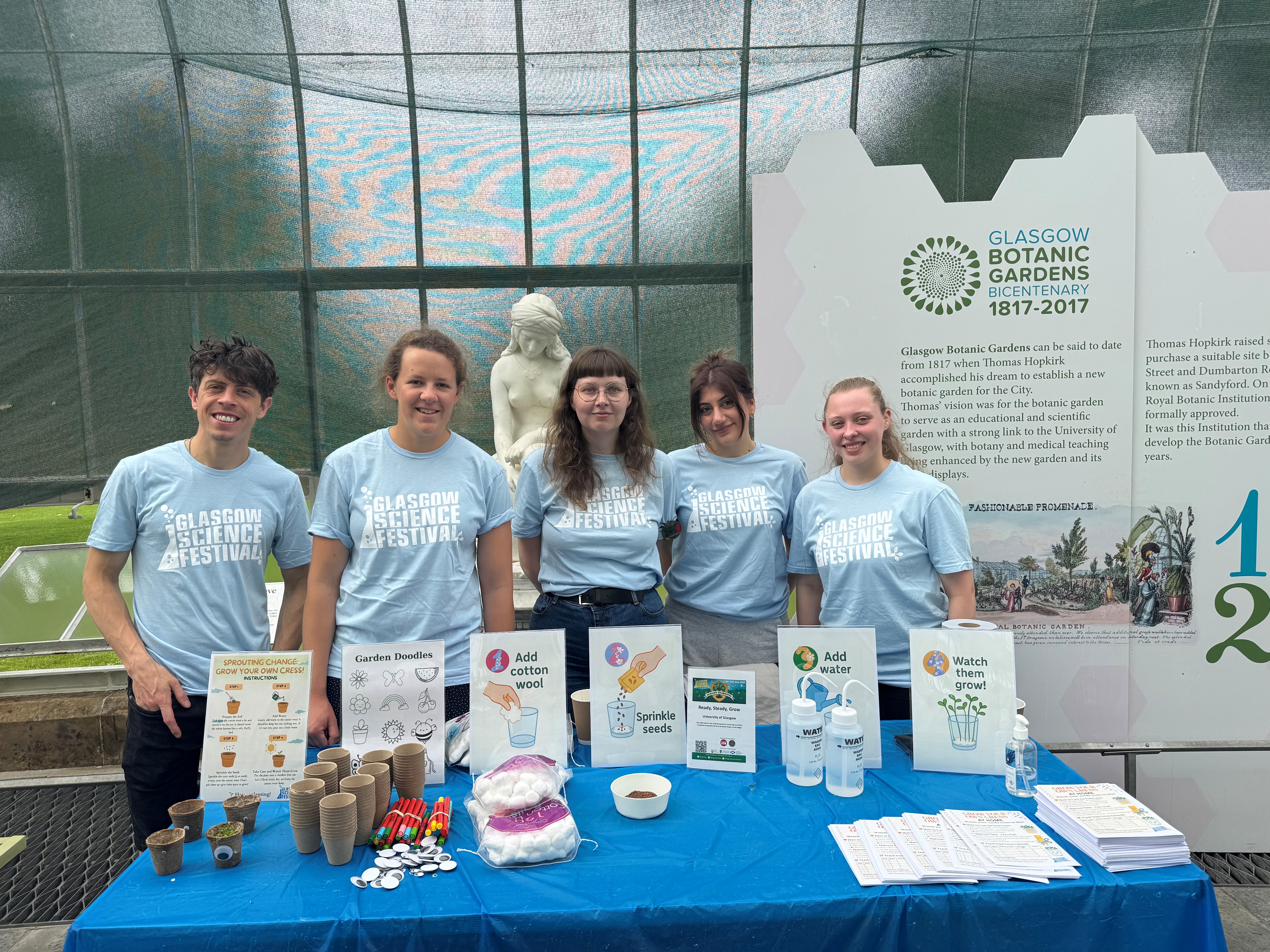Five people in GSF Tshirts standing behind a table with a planting activity