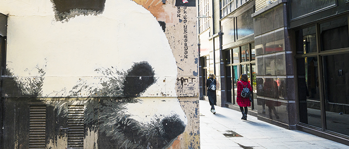 Photograph of street art mural with a panda looking round a street corner as shoppers pass by in the distance