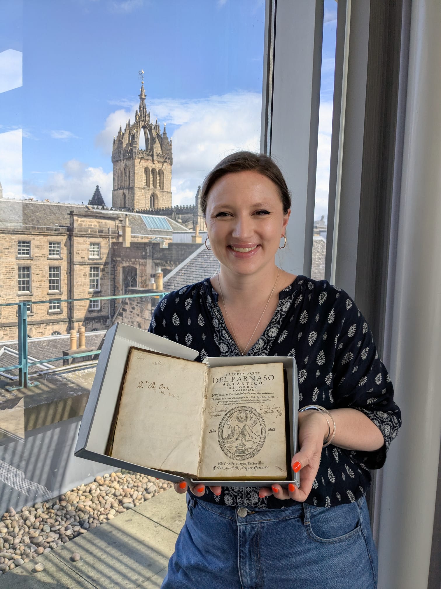 Dr Maya Feile Tomes smiles and holds out an original C17th copy of 
