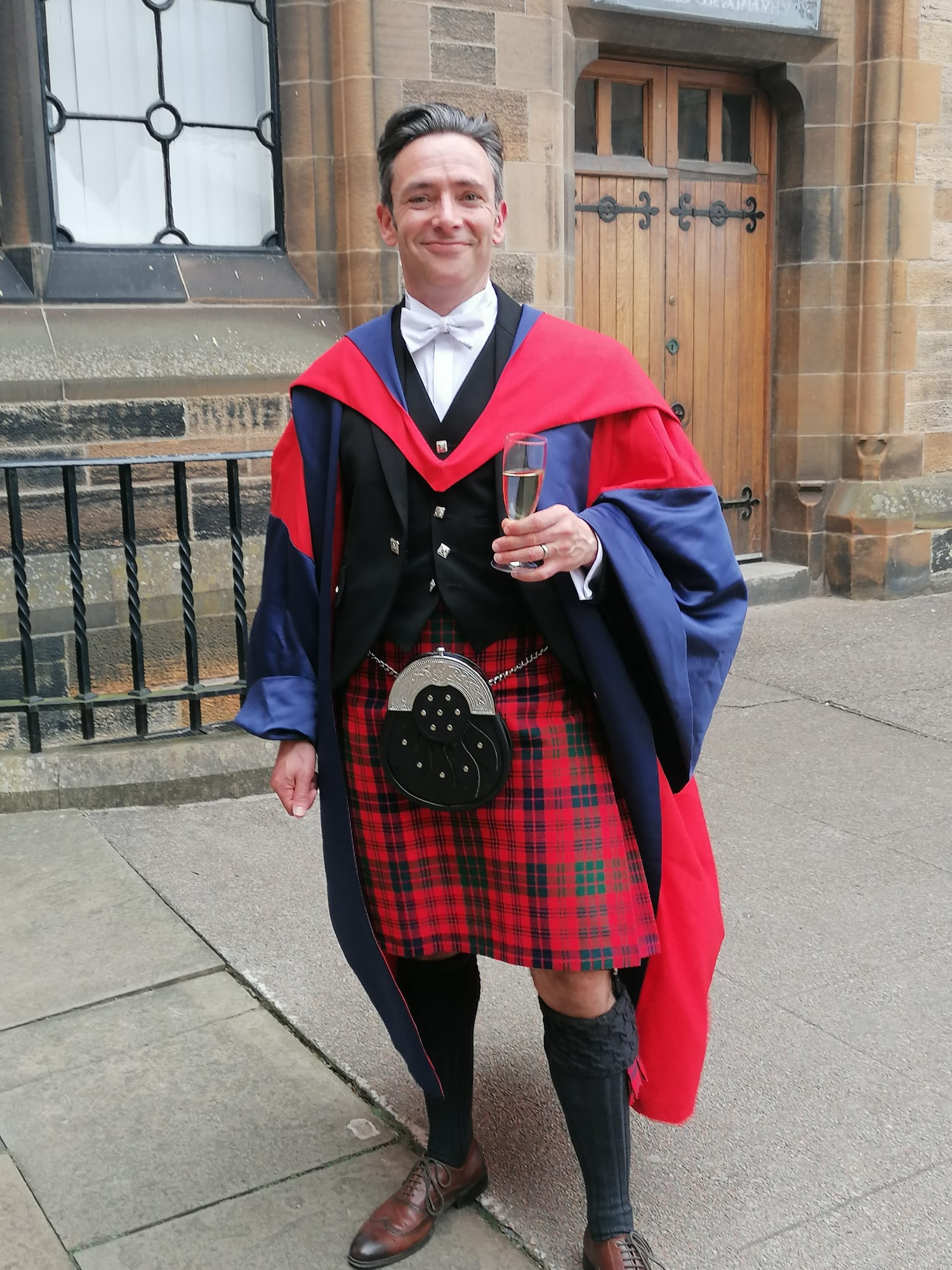 Professor Stephen Forcer stands in the cloisters wearing academic dress.