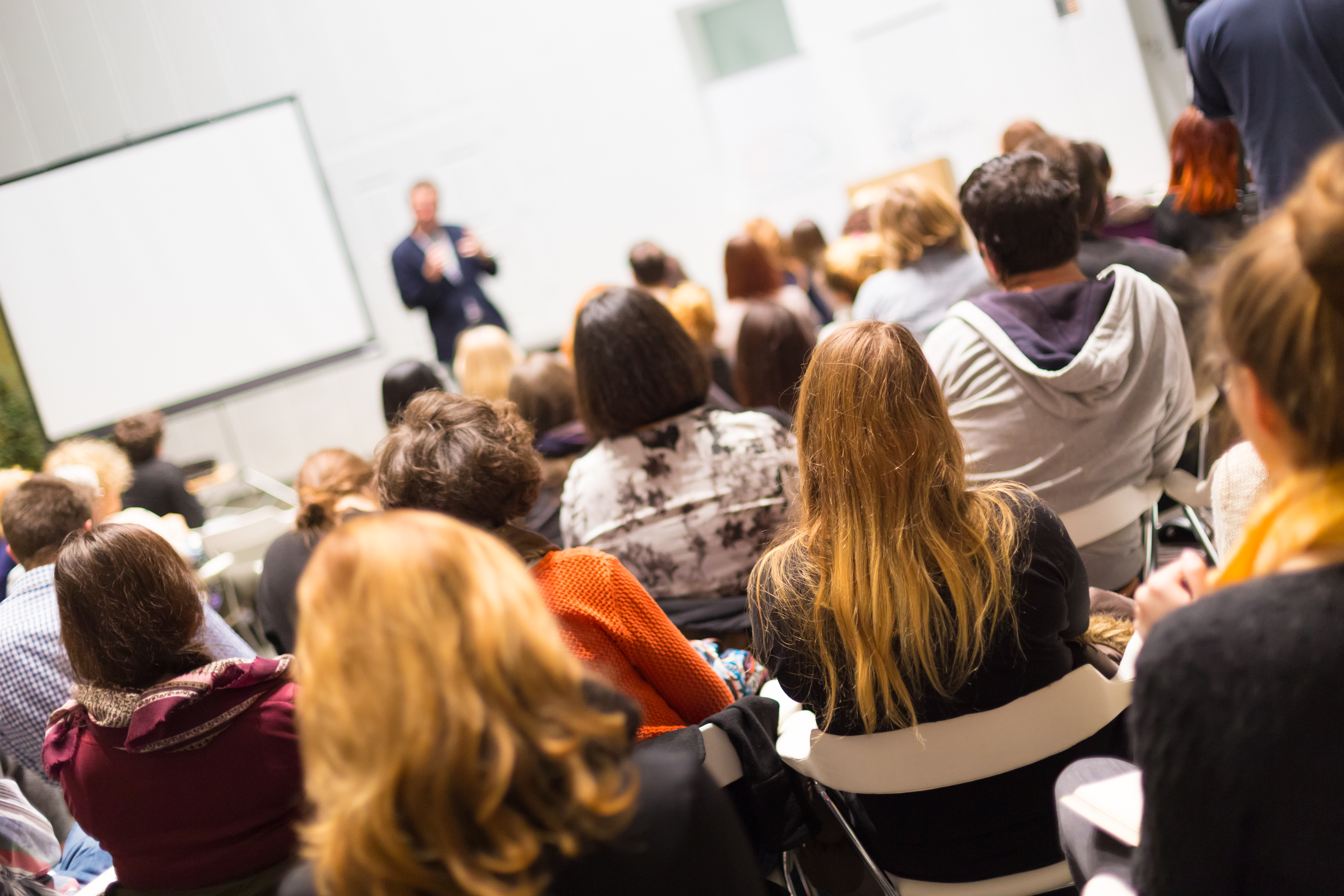 A group of people sit watching a man speaking