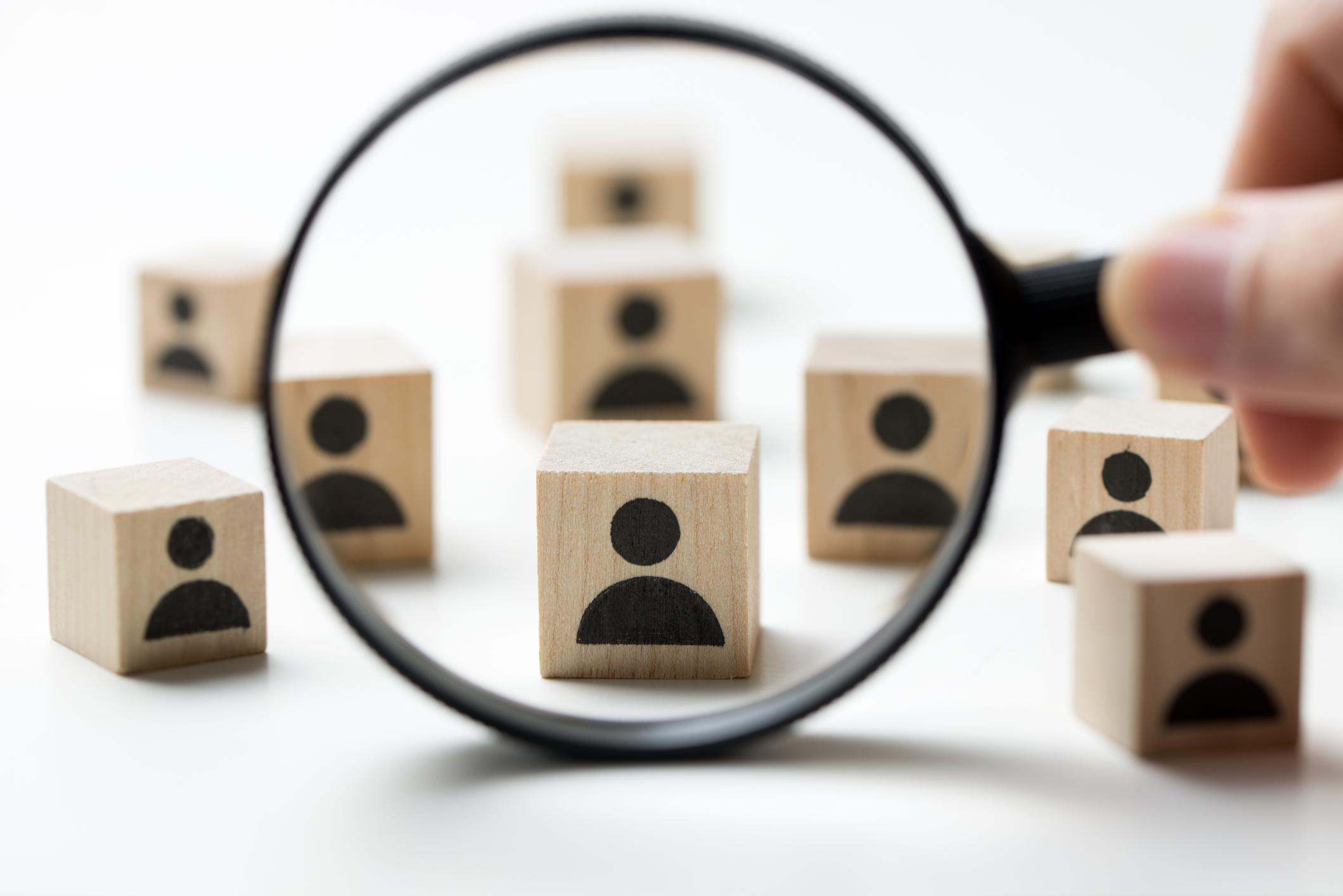A magnifying glass in front of wooden blocks with icons of people on them