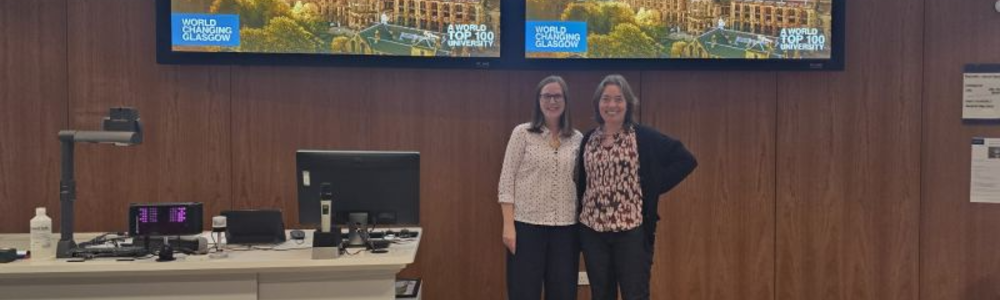 Professor Nicola Veitch stood side by side with Sii Director of Education Professor Olwyn Byron after delivering her inaugural lecture. The pair are stood in the wood-panelled lecture theatre to the left left of the lectern and below the double screen mounted on the wall.