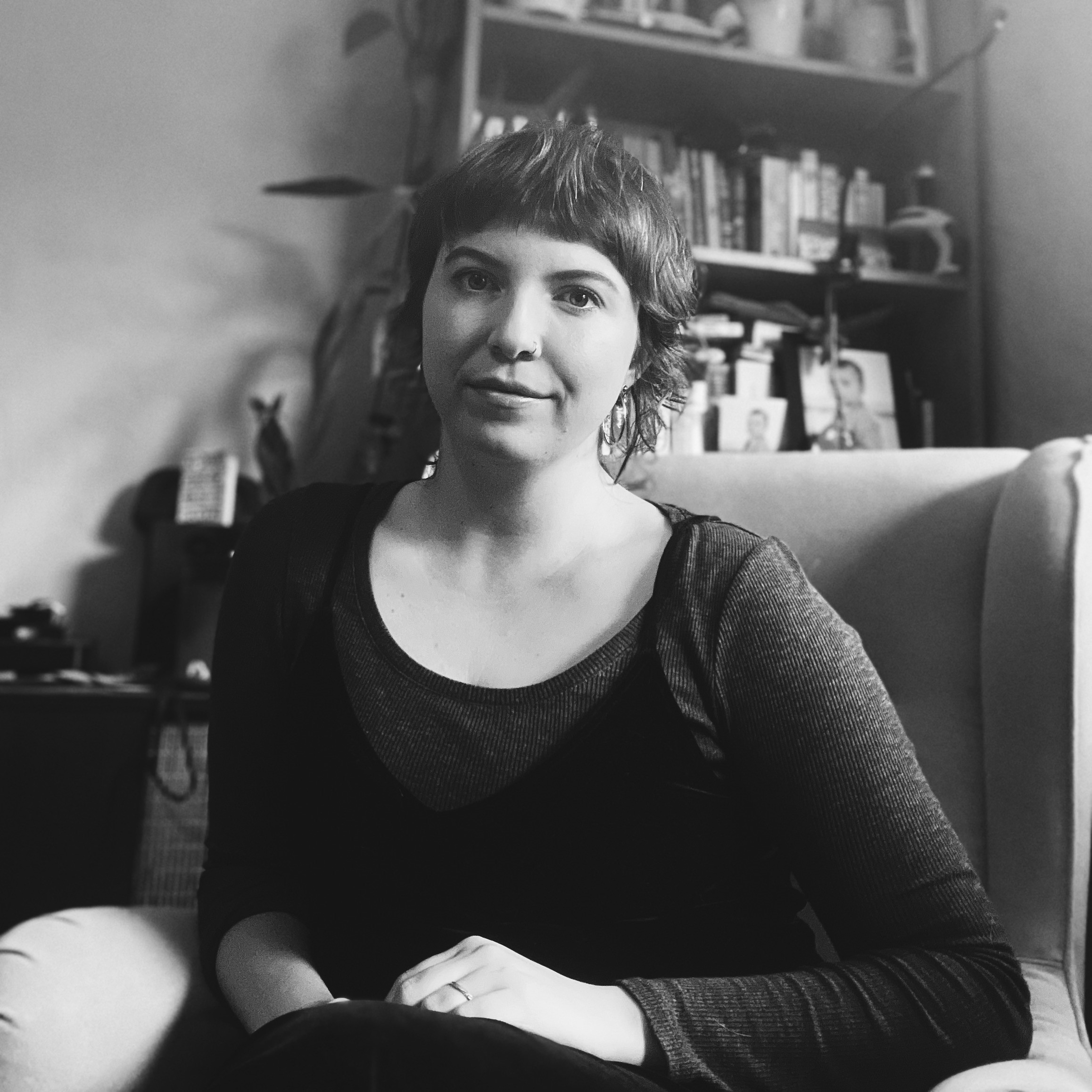 A white woman with brown hair and a fringe sits in an armchair.