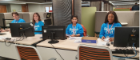 Four students sitting behind desks with computers in front of them smiling at the camera