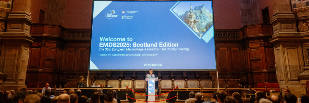 Dr Calum Bain stood at the podium in front of a large screen, introducing the meeting and welcoming delegates