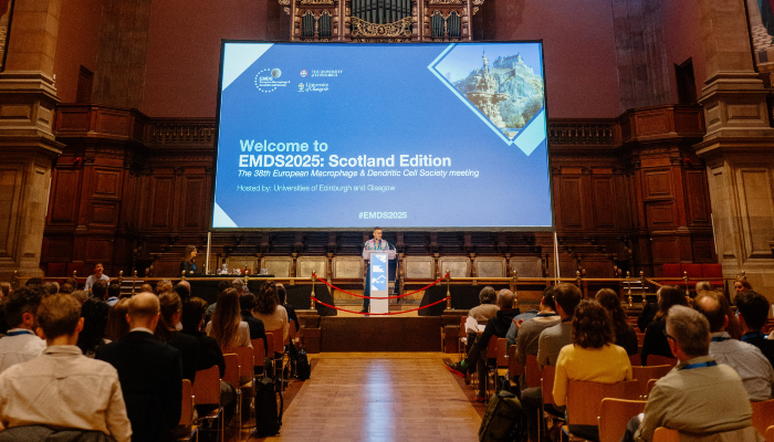 Dr Calum Bain stood at the podium in front of a large screen, introducing the meeting and welcoming delegates