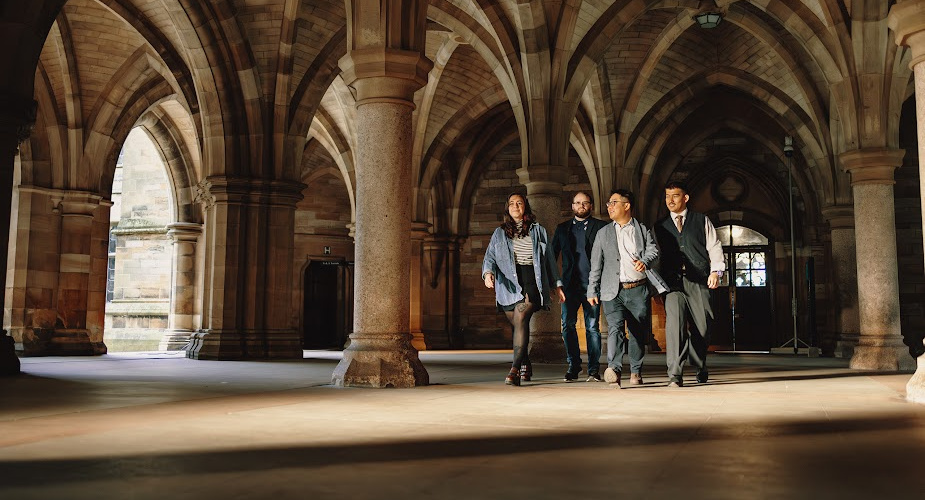 Dr Mark Wong walking through the University of Glasgow's cloisters, talking to three colleagues who are walking alongside him