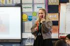a teacher holds up two sticks of coloured cubes, explaining to their class.