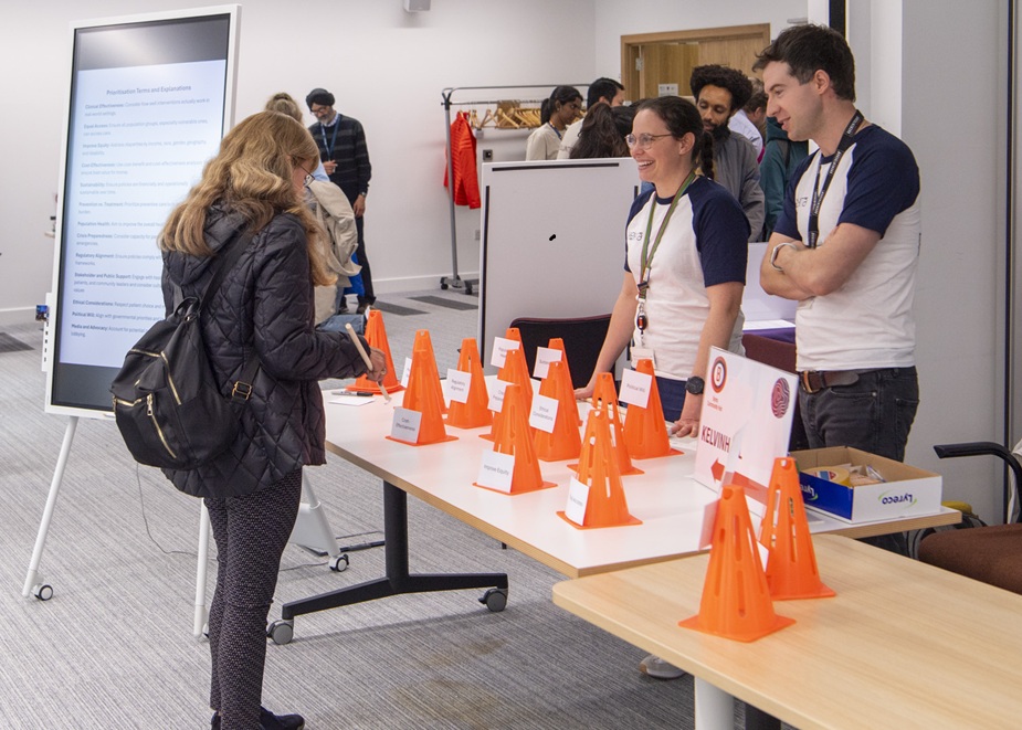 A public engagement activity at the Community Day. Two researchers are standing behind a table with orange cones on it talking to a visitor.