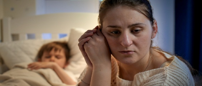 Worried parent sits beside a sleeping child