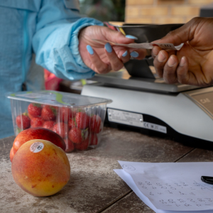 A close up on someone handing the cashier a note to pay for the strawberries and apple sitting on the counter.