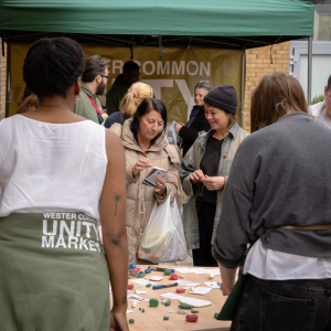 Two members of staff facing away from the camera standing by a table with clay models. In the gap between them you can see two customers holding the clay smiling and chatting.