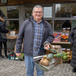 A customer smiling happily at the camera while holding a full basket of vegetables.