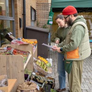 Two members of staff looking at a list and checking the shelves of veg.