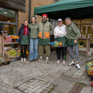 A group of people standing in front of the till and smiling at the camera. Two of them are wearing Unity Market jumpers and one two have market aprons on.