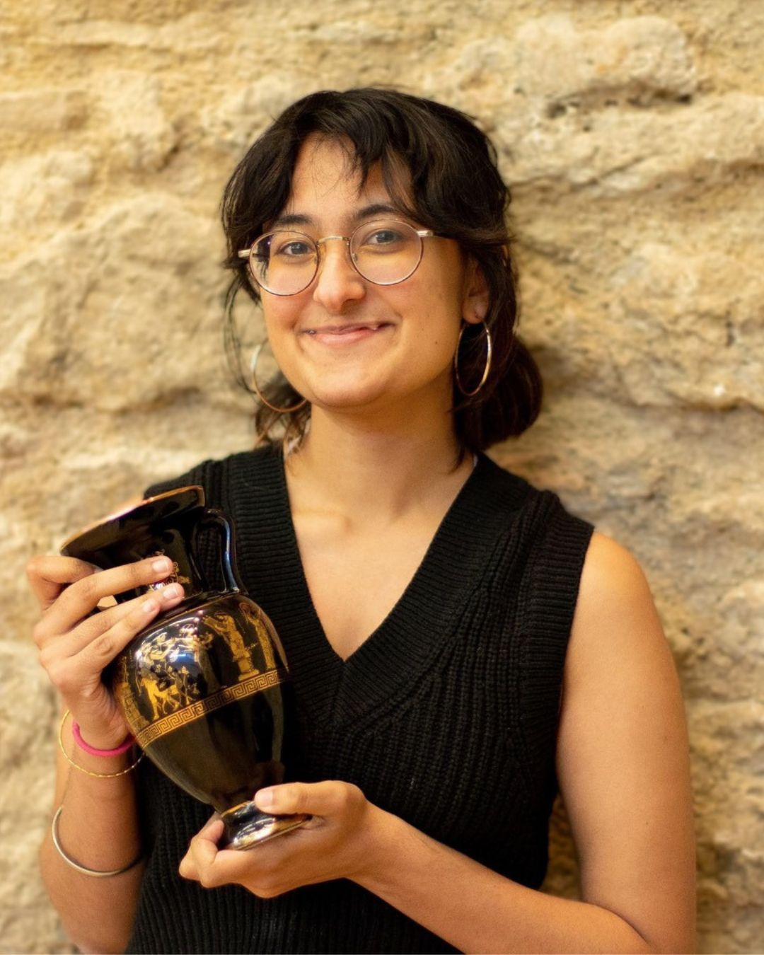 Photograph of Sav Sood. They are smiling and holding a Greek style mini amphora.