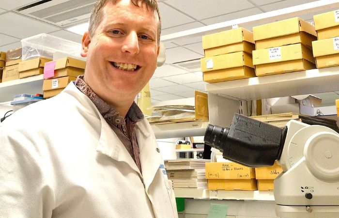 A man smiling next to a microscope