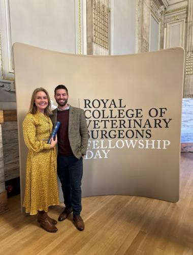 Image of Katie Denholm holding her award next to a male of unknown identity in front of the RCVS Fellowship Banner