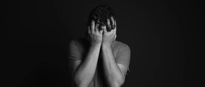 A black and white photo of a man holding his face in his hands in a black room