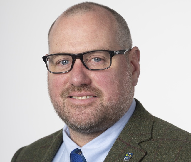 A portrait of a man wearing a shirt, tie and jacket looks into the camera