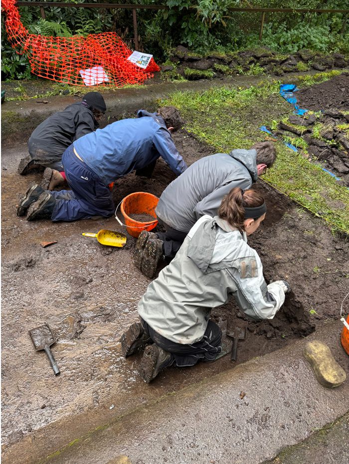 Students clean back surface in trench