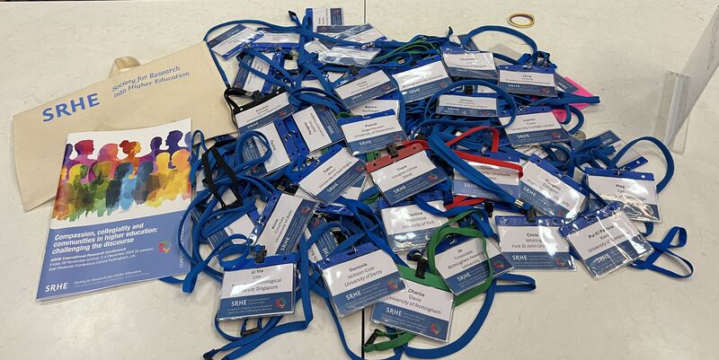 Conference registration badges and lanyards arranged on a table alongside SRHE materials, including a programme booklet themed around compassion, collegiality, and community, representing delegate participation and engagement at the SRHE Conference.
