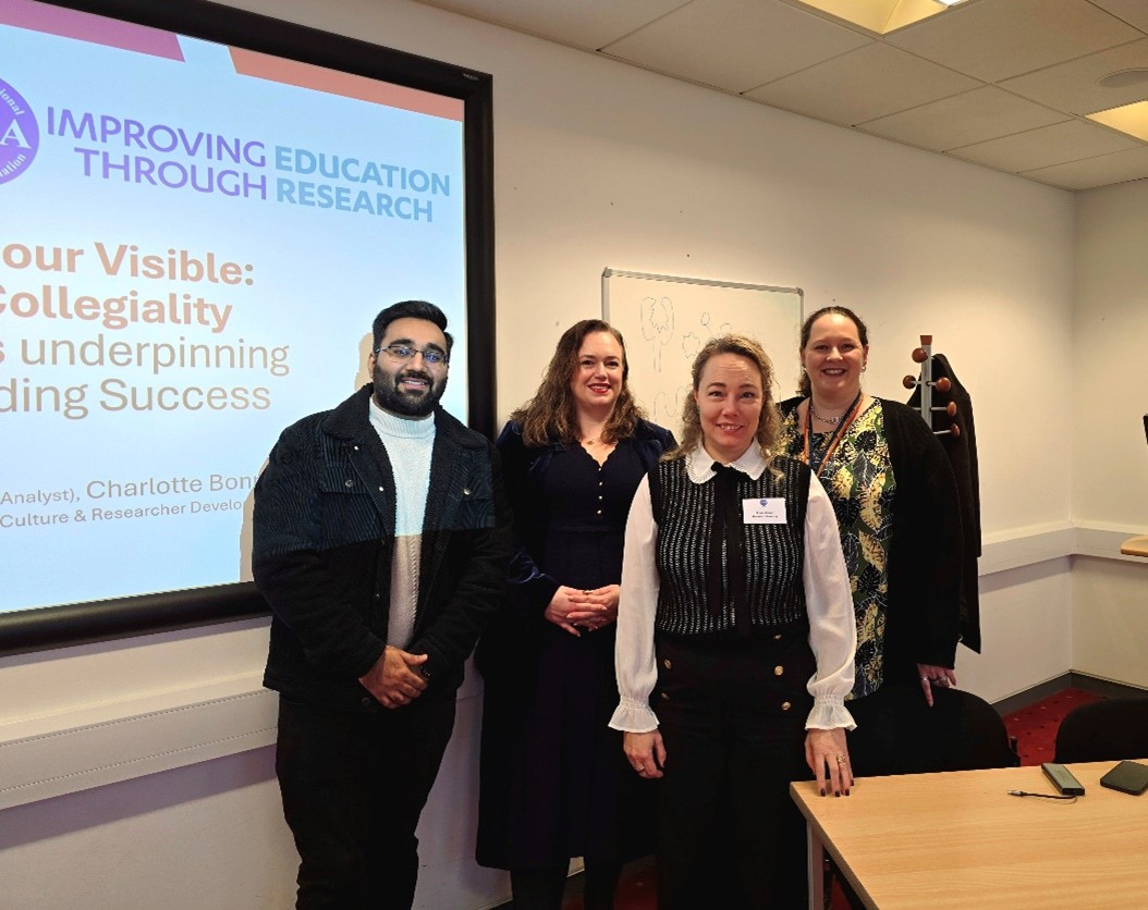 Group of speakers standing at the front of a conference room following a presentation on improving education through research and collegiality. A projected slide behind them references visible and underlying factors that support learning success, with the setting reflecting formal knowledge exchange and collaboration in higher education.