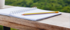 Open notepad and pencil resting on a wooden desk with a green landscape in the background