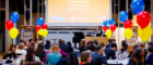 A photo of the Student Teaching Awards Ceremony with people sitting at tables, multi-coloured balloons and a stage.