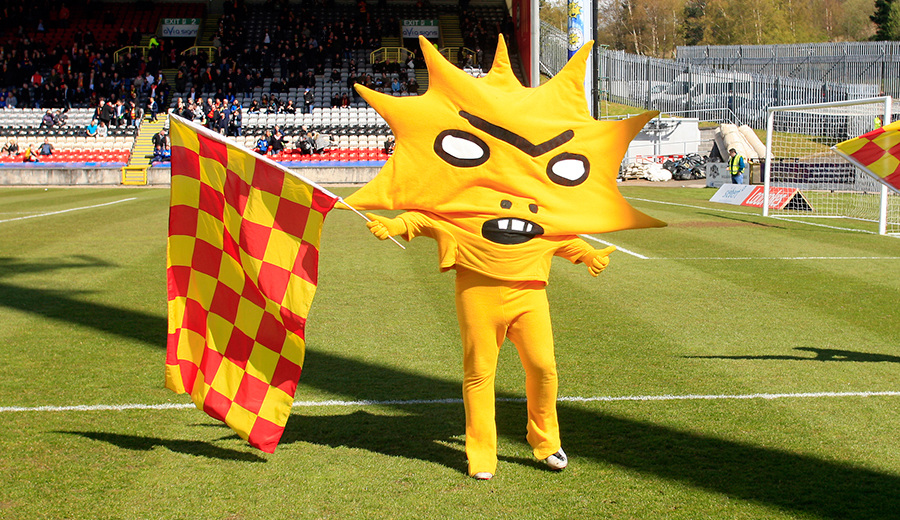 Partick thistle mascot Kingsley (a yellow sun-like figure) stands on the grounds of Firhill stadium
