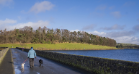 the milngavie reservoir, a large body of water with a bridge to the left of the frame. A person and a dog walk away from the camera