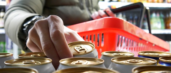 A supermarket shopper is reaching for a can to put in their red basket