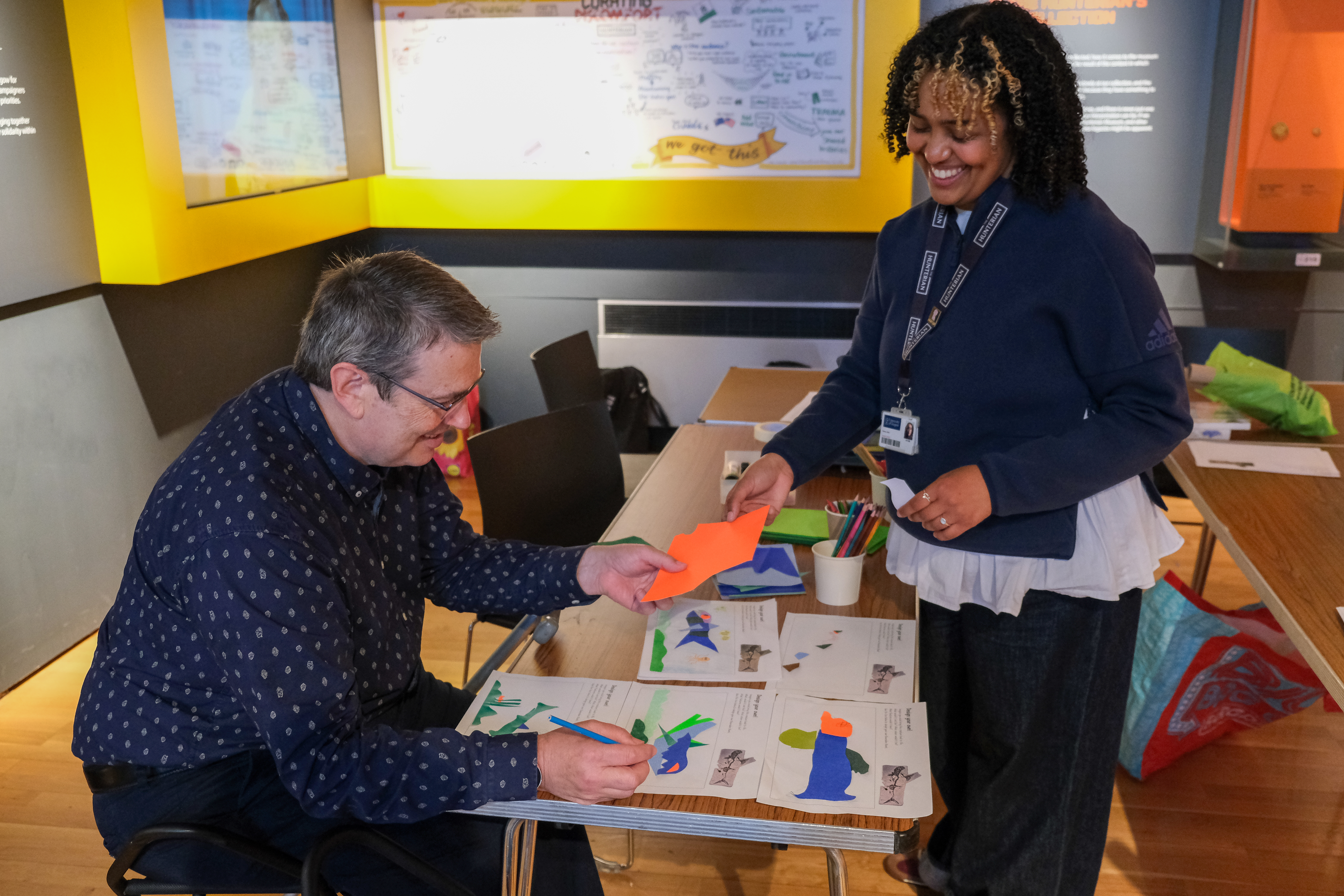 Eleni in the Hunterian museum standing while a man sits doing crafts