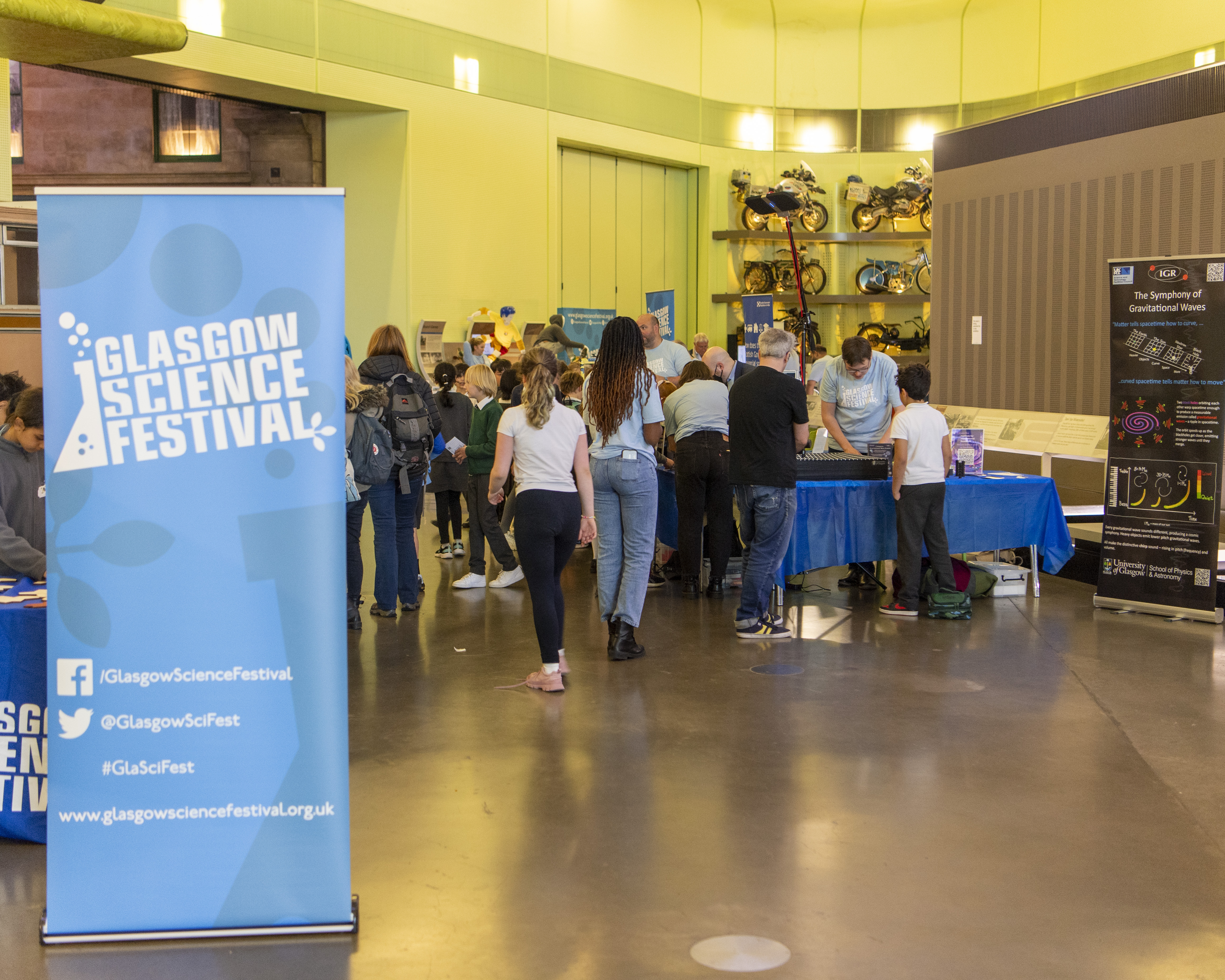 A Glasgow Science Festival Banner and in the background is a crowd of people in the Riverside Museum