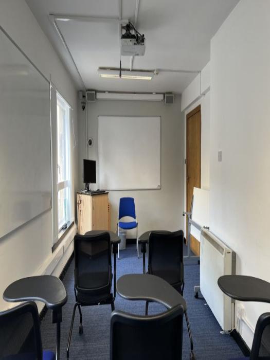 Flat floored teaching room with tablet chairs, whiteboard, projector, PC, and lecturer's chair.