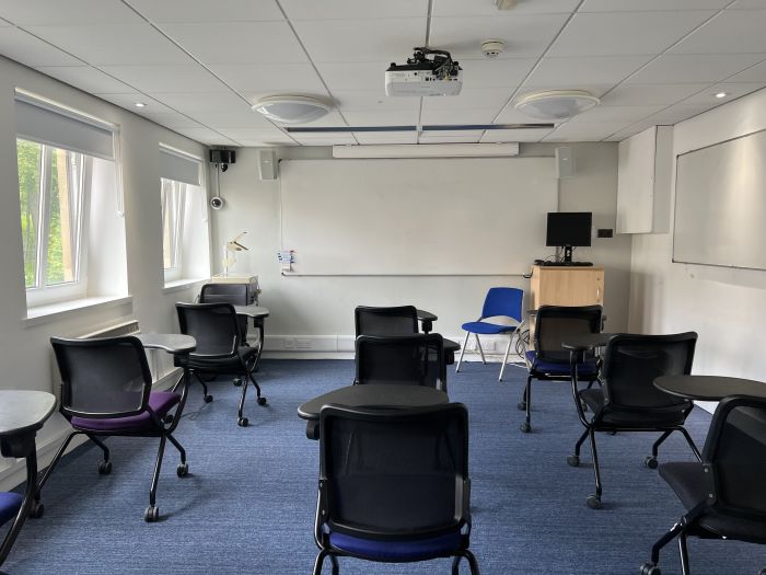 Flat floored teaching room with tablet chairs, whiteboards, projector, PC, visualiser, and lecturer's chair.