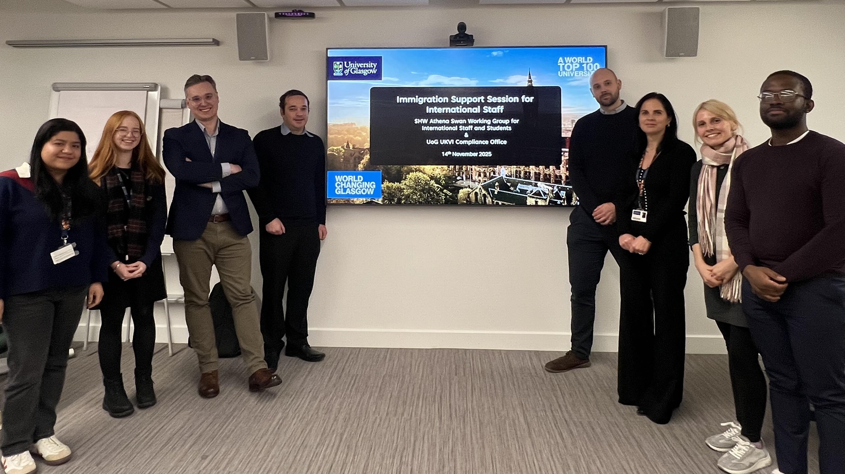 University colleagues standing either side of a large screen. The screen has a slide with the title 'Immigration session for international staff'