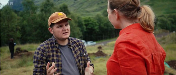 Two people discuss the excavation at Glencoe while people dig in the trench behind them