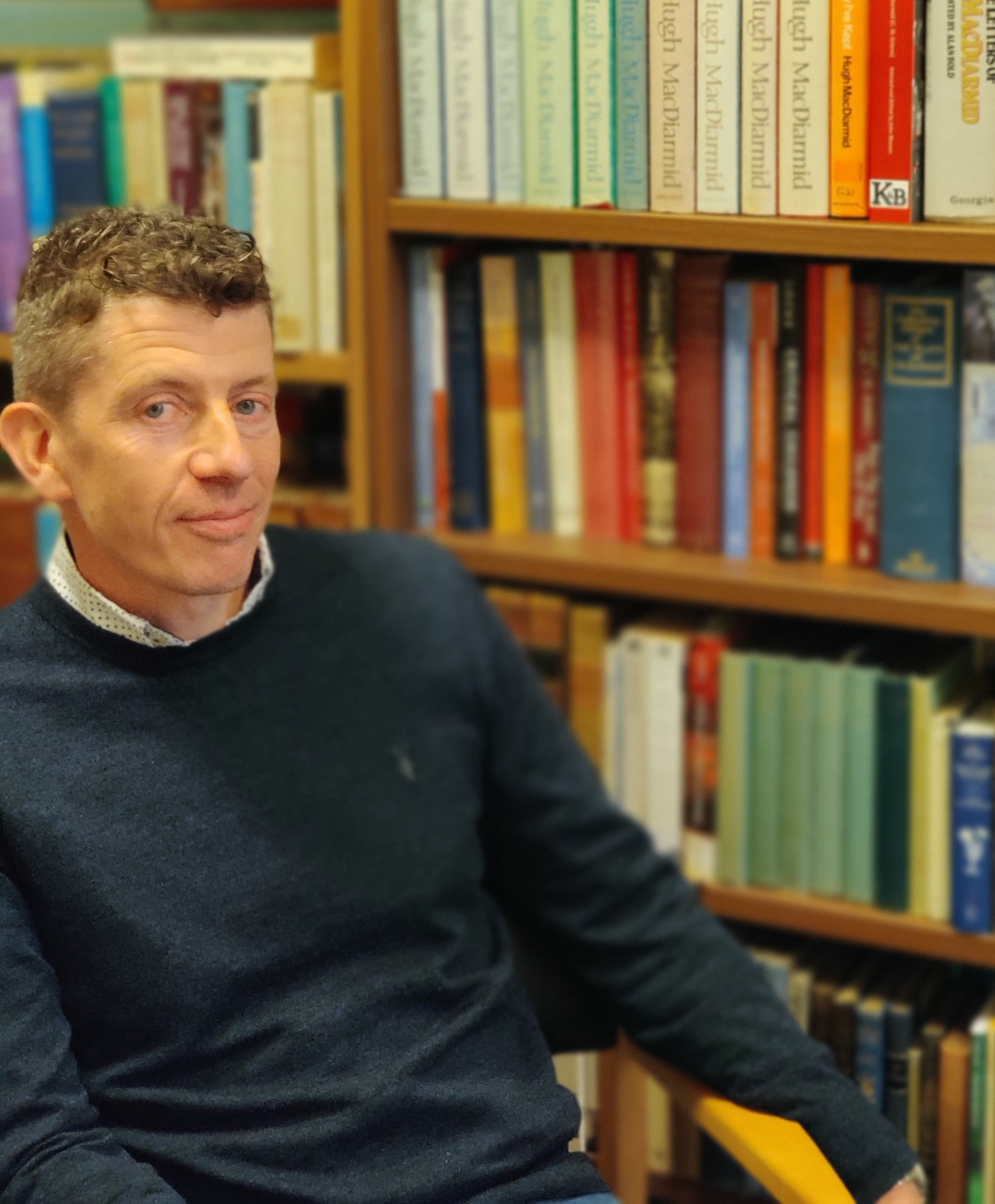 A picture of Andrew Nash sitting on a chair in front of a bookcase