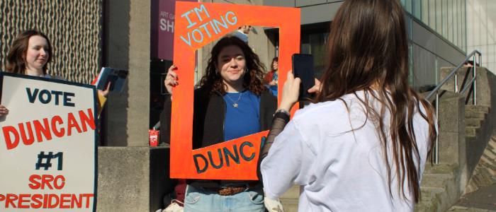 A student posing for a photo with a banner around her saying 