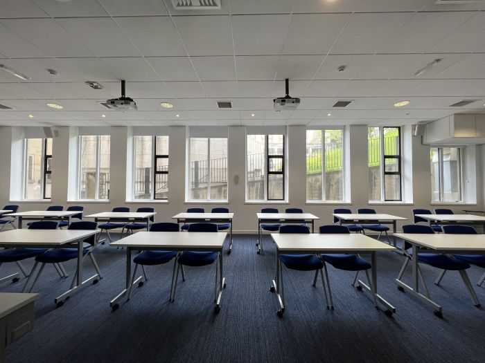 Flat floored teaching room with rows of tables and chairs, and projectors.