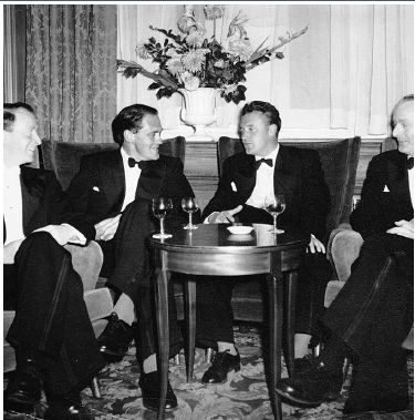 Image of Bill Jarrett and colleagues sitting round a table with drinks wearing dinner suits