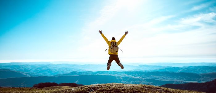 Man jumping on hill side looking at clouds