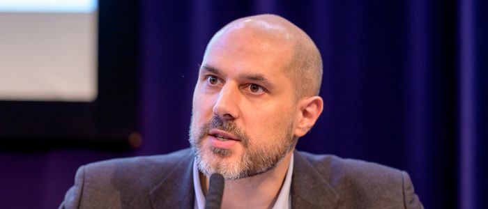 Bearded man talking into a microphone at an interview